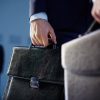 Cropped image of business partners carrying briefcases on the foreground while their colleague standing on the background