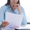 Closeup of woman holding and reading document. Entrepreneur sitting at desk and working. Paperwork and management concept. Cropped view.